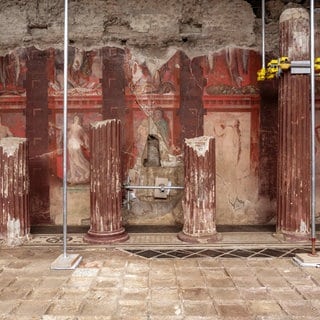 Antike Fresken des Dionysos-Kults in einer römischen Villa in Pompeji. Rötliche Wandmalereien zwischen teilweise erhaltenen Säulen zeigen Einweihungsrituale der dionysischen Mysterien.